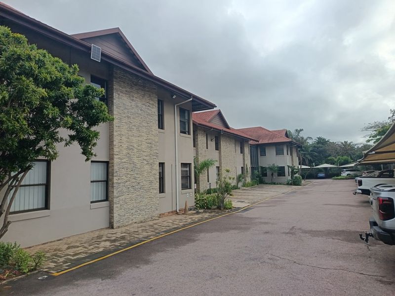 A multi-story office building featuring stone cladding, tiled roofing, and an extensive paved driveway with covered parking facilities.