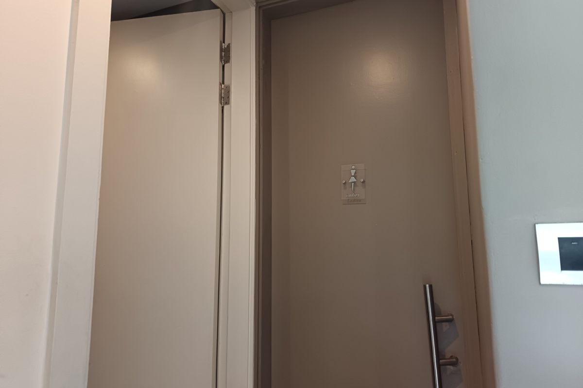 A view of a bathroom entrance door featuring modern lever handle hardware and clear signage.