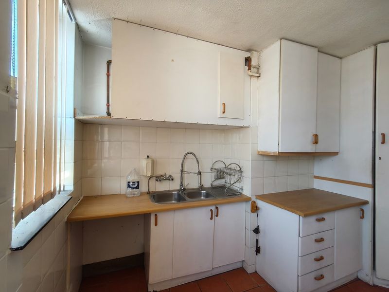 A dated kitchen featuring white cabinetry, laminate countertops, a double bowl sink, and tiled backsplash, offering significant potential for modernization and renovation.