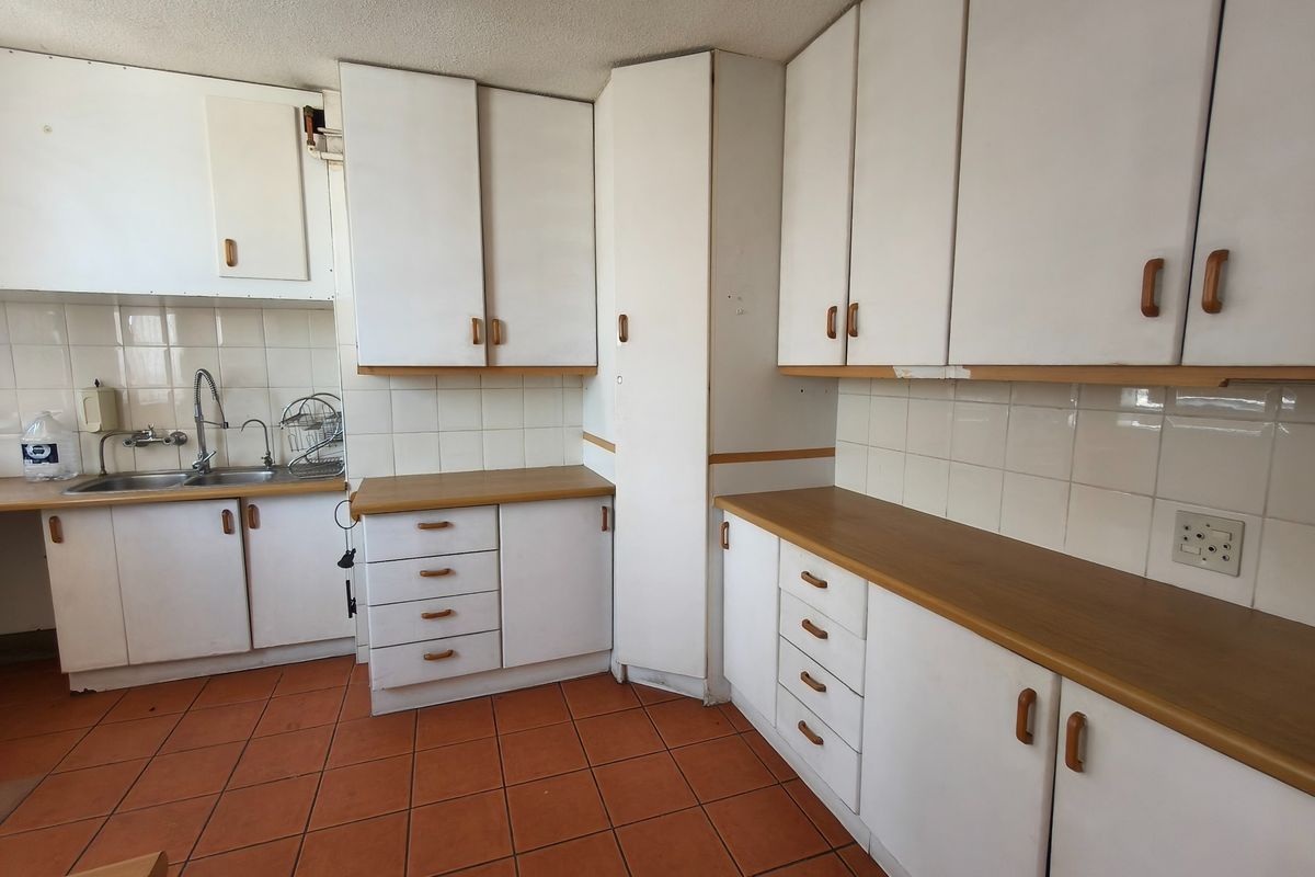 A dated kitchen featuring white cabinetry, laminate countertops, tiled backsplash, and ceramic floor tiles, offering a blank canvas for renovation.