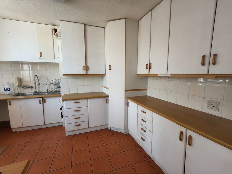 A dated kitchen featuring white cabinetry, laminate countertops, tiled backsplash, and ceramic floor tiles, offering a blank canvas for renovation.
