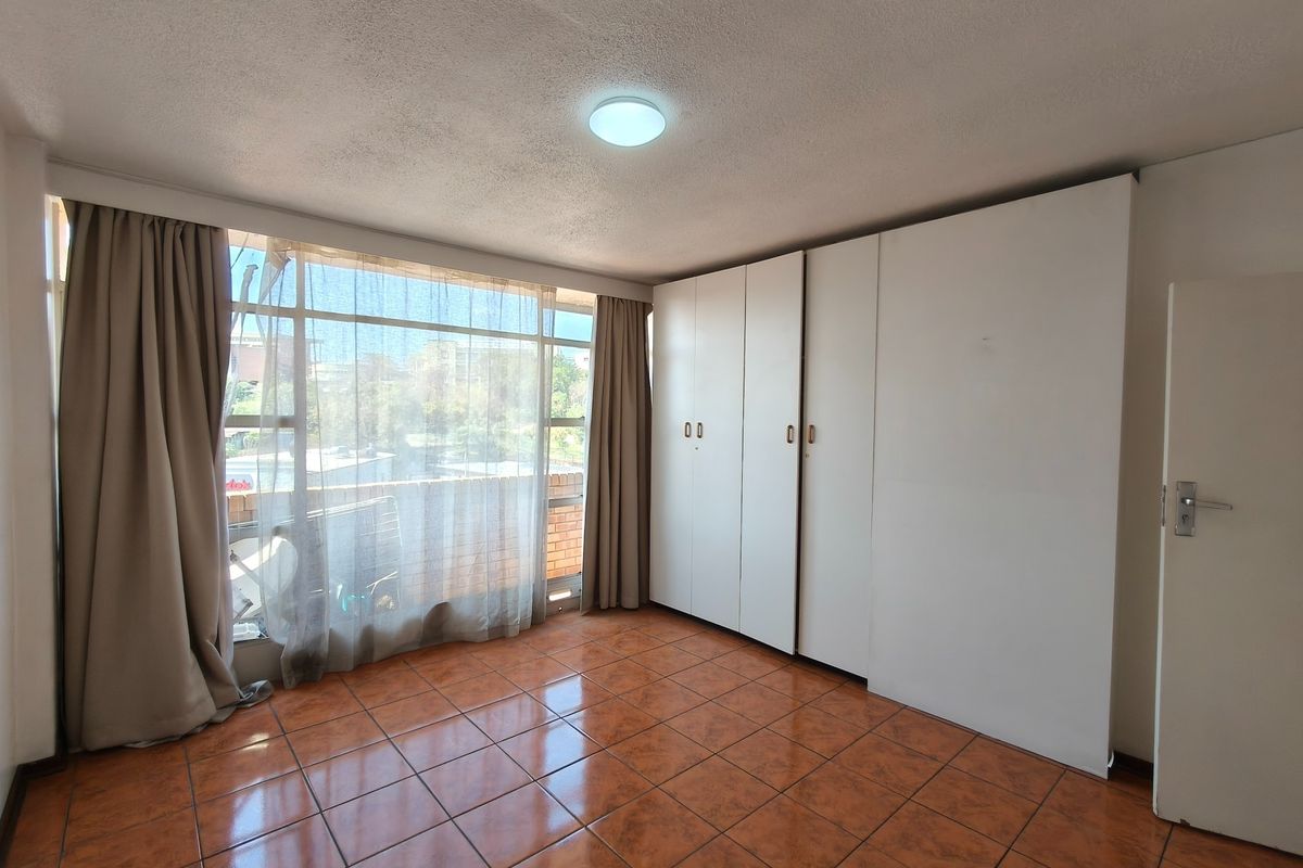 A bright, empty bedroom featuring tiled flooring, large windows with natural light, and ample built-in cupboard storage space.