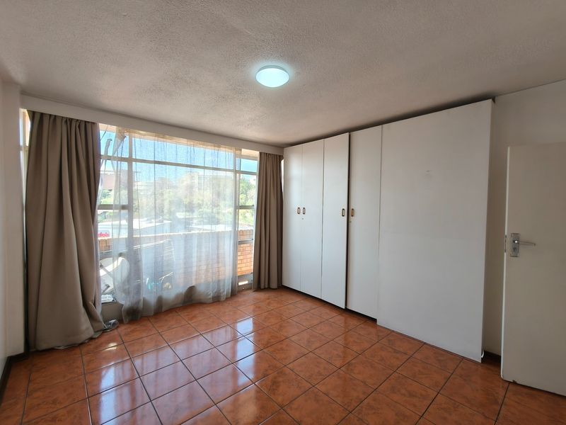 A bright, empty bedroom featuring tiled flooring, large windows with natural light, and ample built-in cupboard storage space.