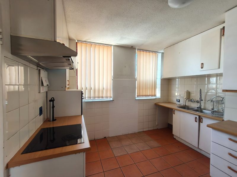 A functional kitchen featuring built-in cabinetry, laminate countertops, an electric hob, and tiled flooring, offering a blank canvas for modern renovation.