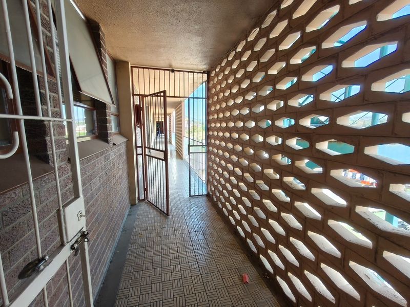 An outdoor apartment access walkway featuring a decorative breeze block screen wall, security gate, and tiled flooring.