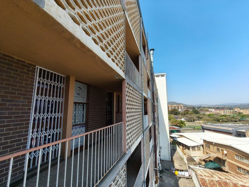 Exterior view of an apartment building featuring a brick facade, decorative breeze block screens, and metal security gates along the walkway.