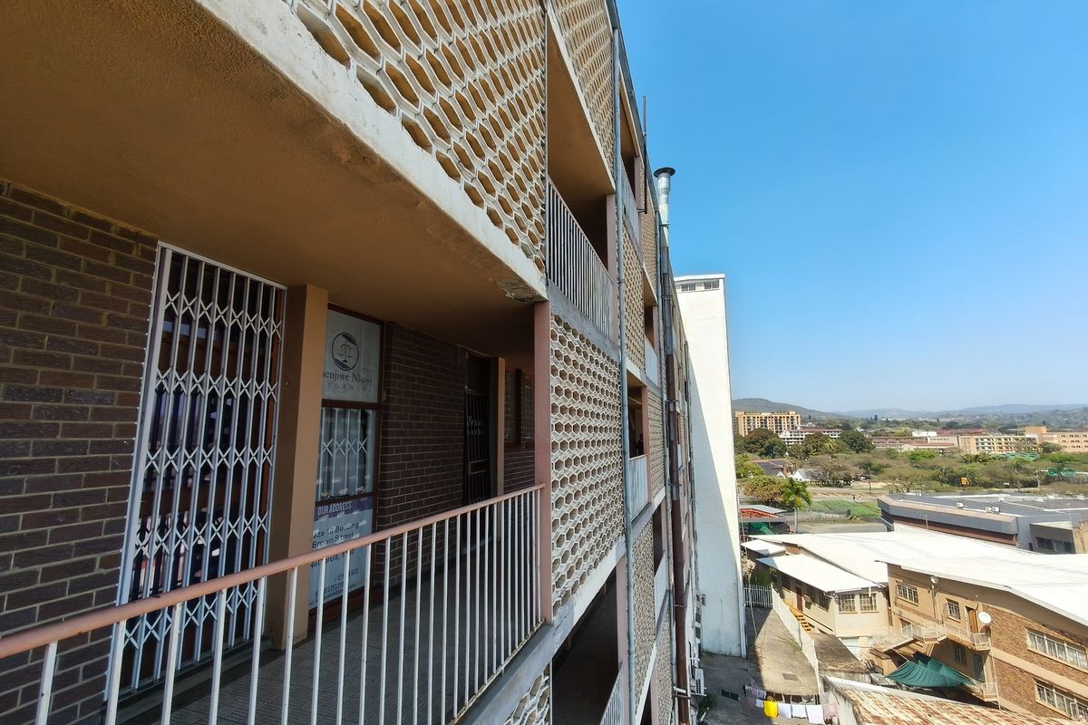 Exterior view of an apartment building featuring a brick facade, decorative breeze block screens, and metal security gates along the walkway.