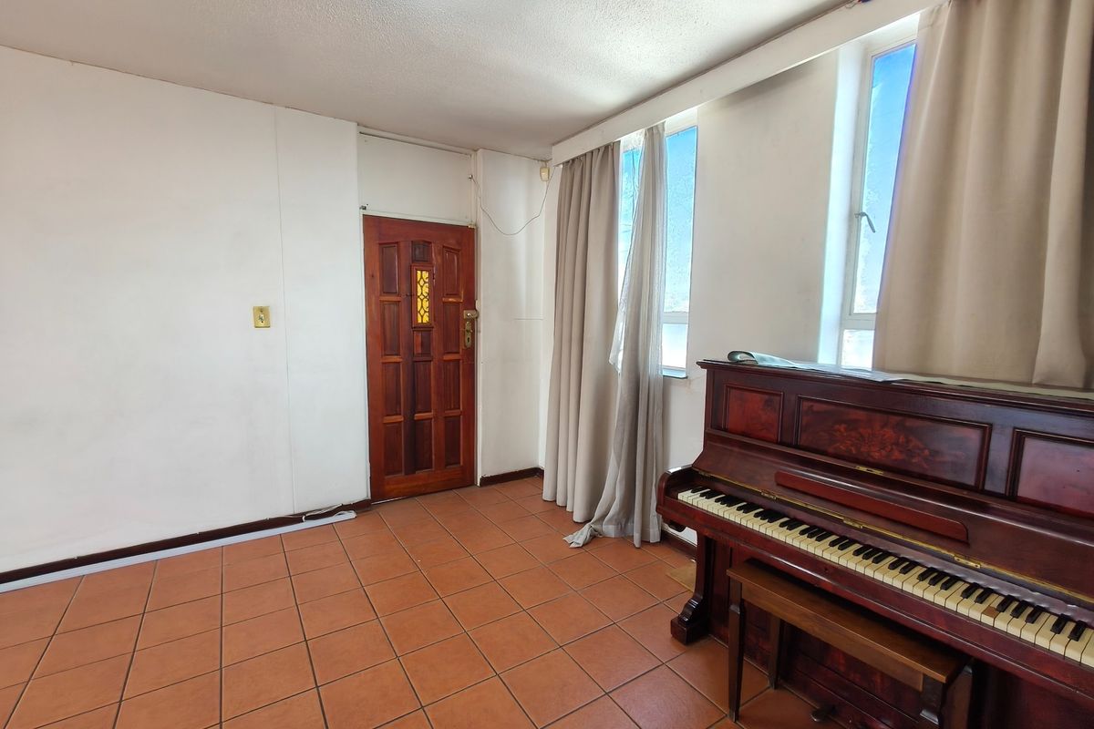 A living area featuring terracotta-style tiled flooring, a solid timber entrance door, and large windows allowing natural light into the space.