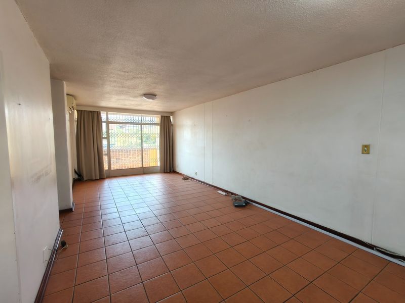 An empty, open-plan living area featuring terracotta tiled flooring, a security gate, and a sliding glass door leading to an outdoor space.