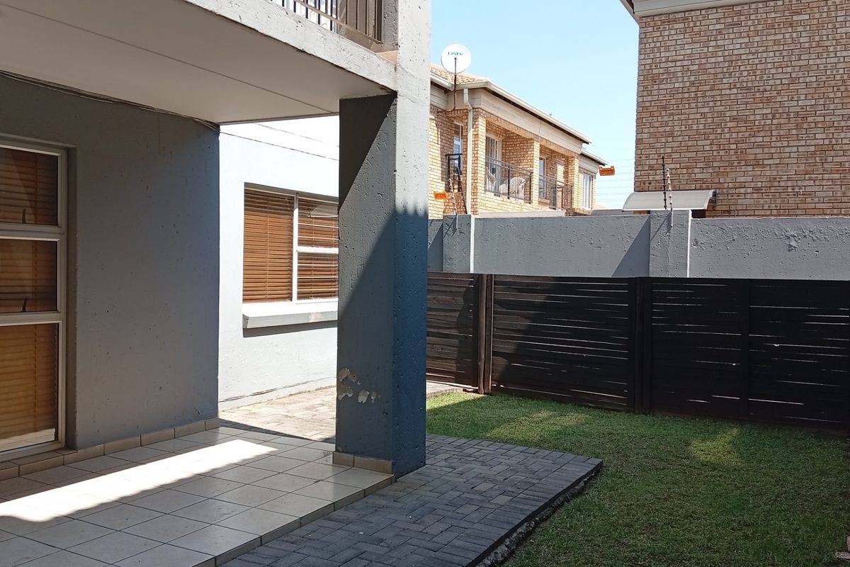 A private rear courtyard featuring a covered tiled patio, paved walkway, small lawn area, and secure boundary fencing.