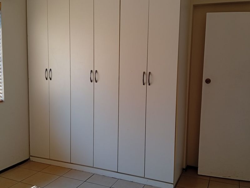 A clean, empty bedroom featuring neutral tiled flooring, built-in white cupboards, and venetian blinds on the window.