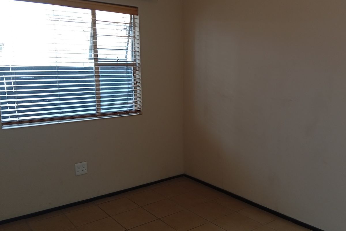 An empty bedroom featuring tiled flooring, neutral walls, and a window fitted with venetian blinds.
