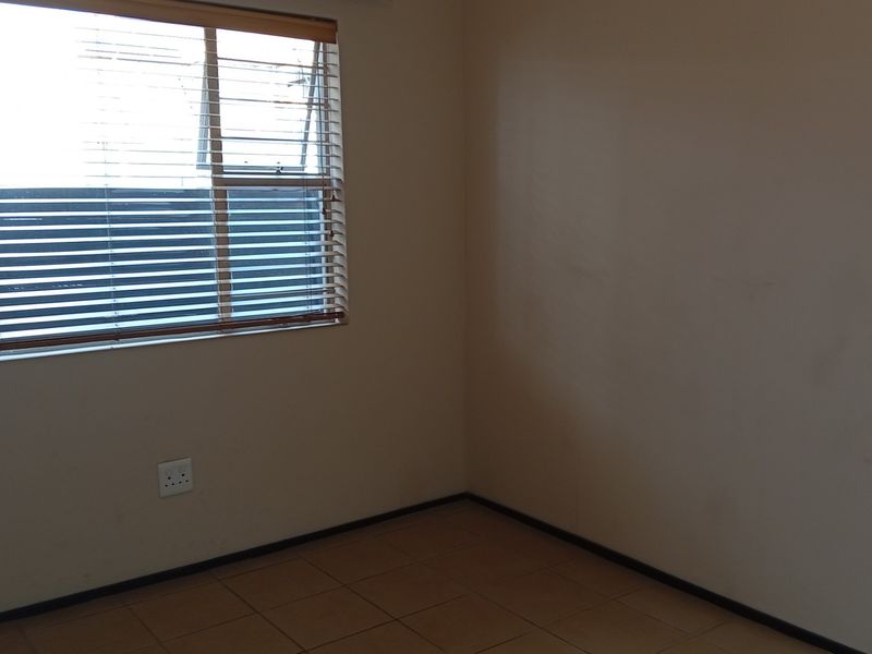 An empty bedroom featuring tiled flooring, neutral walls, and a window fitted with venetian blinds.