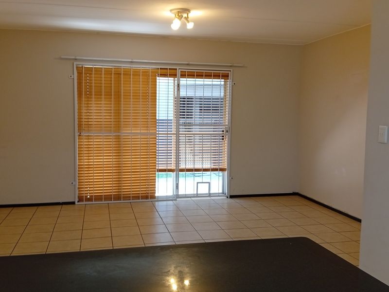 An empty living room featuring tiled flooring, a sliding glass door with security gate, and venetian blinds, providing a clean and neutral space.