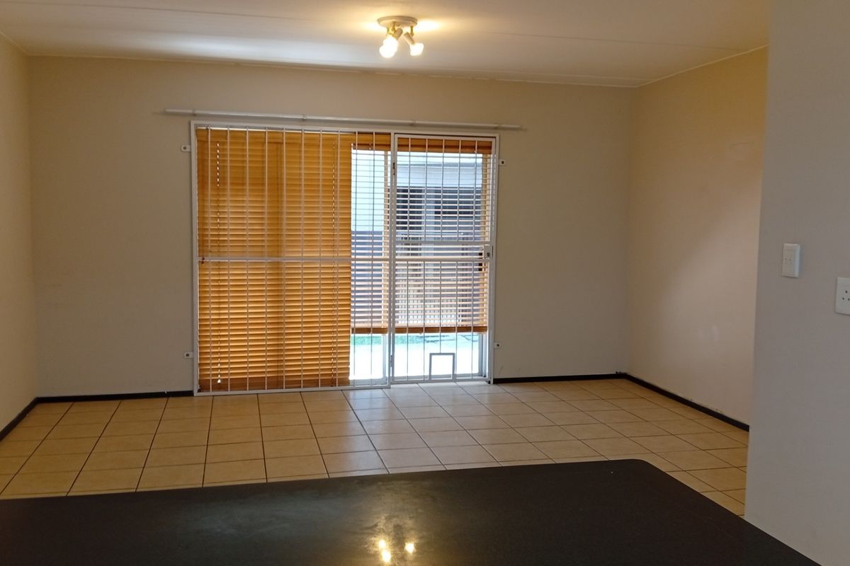An empty living room featuring tiled flooring, a sliding glass door with security gate, and venetian blinds, providing a clean and neutral space.