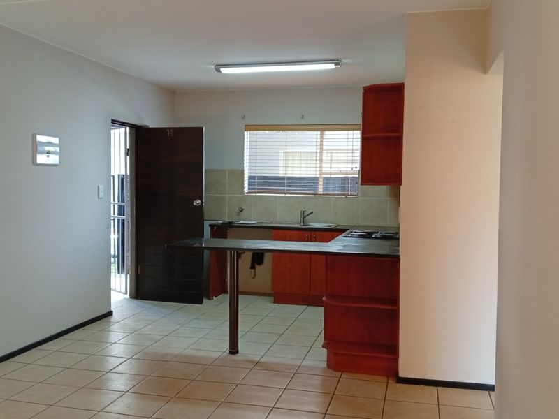 Open plan kitchen area featuring built-in wooden cabinetry, a breakfast bar, tiled flooring, and direct access to an exterior door.