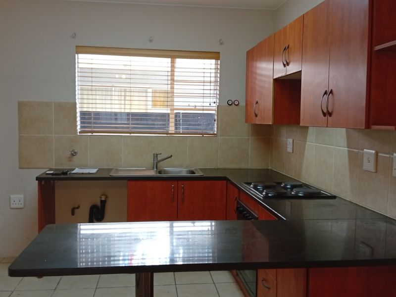 A functional kitchen featuring wooden cabinetry, dark countertops, a built-in hob and oven, and tiled backsplash, offering a clean and practical workspace.