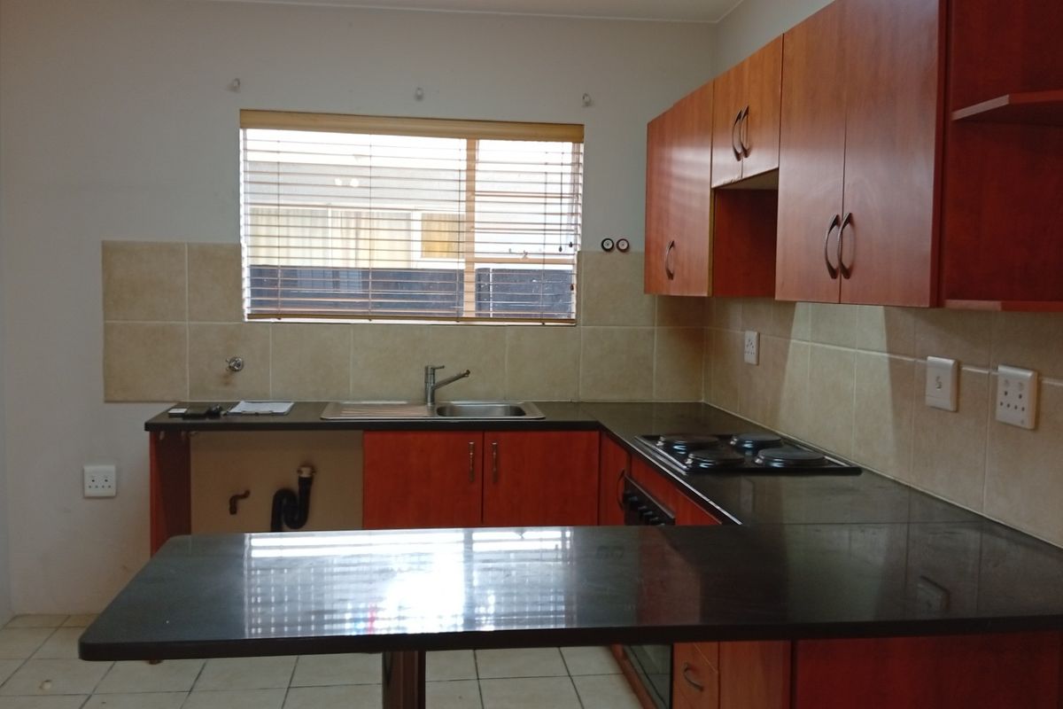 A functional kitchen featuring wooden cabinetry, dark countertops, a built-in hob and oven, and tiled backsplash, offering a clean and practical workspace.
