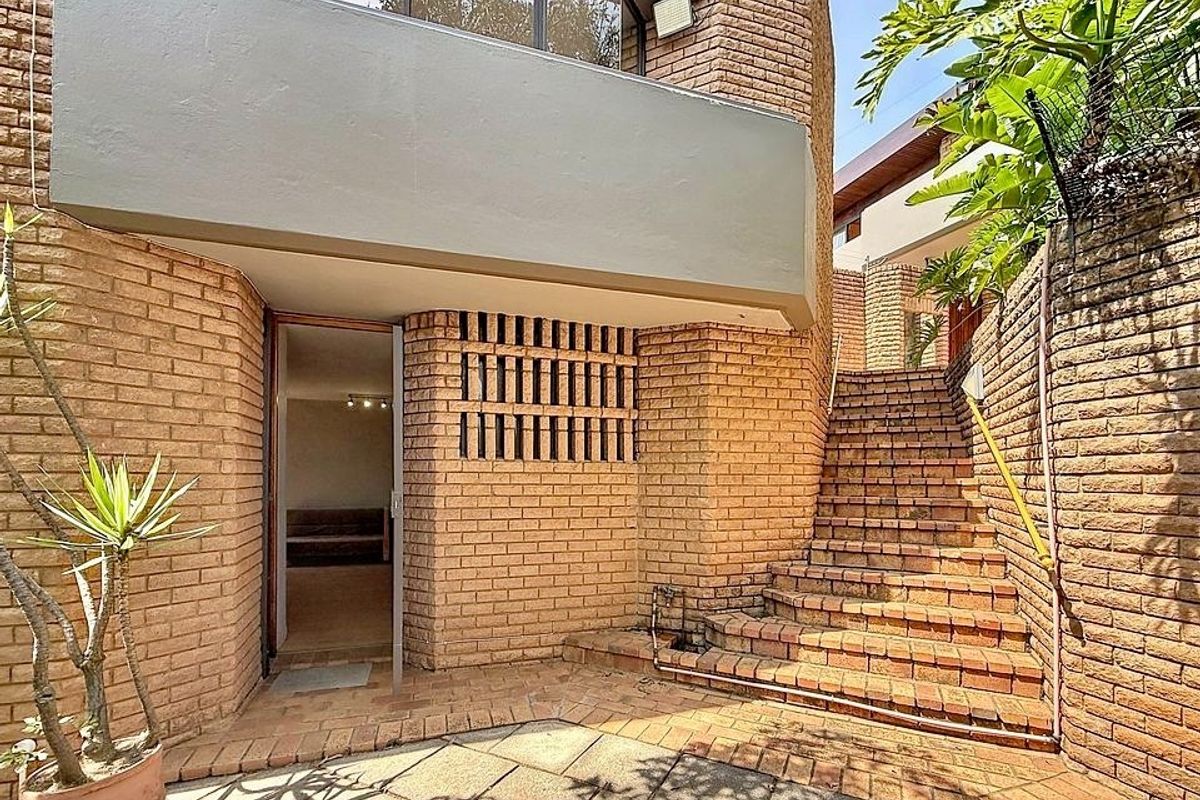 A rear exterior view featuring a brick facade, a paved patio area, and a brick staircase leading to an upper level.