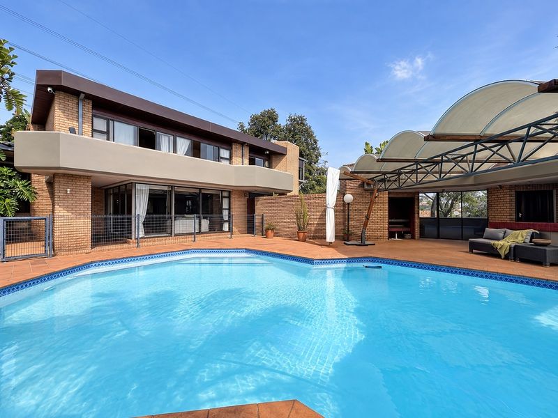 Spacious outdoor pool area featuring a large swimming pool, tiled patio, and a unique curved shade structure set against a brick house facade.