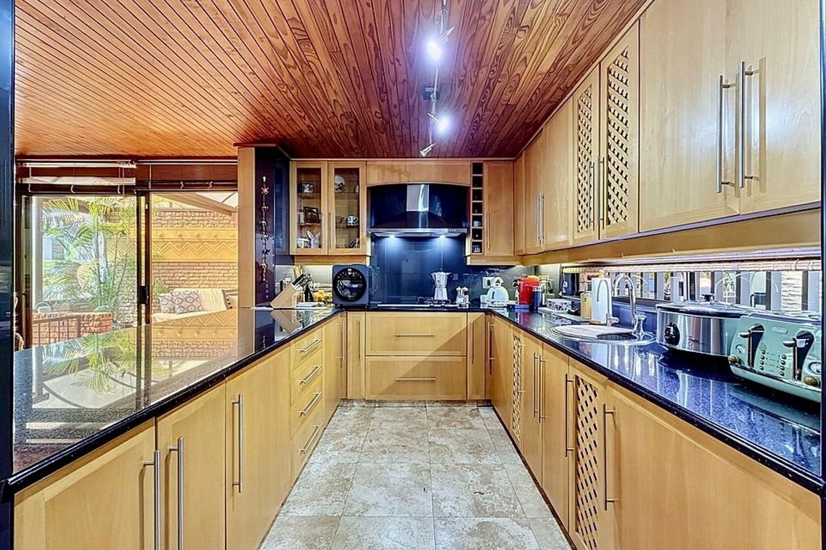 A functional kitchen featuring wooden ceiling paneling, granite countertops, ample built-in cabinetry, and direct access to an outdoor patio area through sliding glass doors.