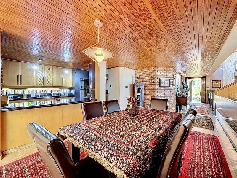 Open-plan dining and kitchen area featuring a distinctive timber-clad ceiling, exposed brickwork, and functional built-in cabinetry with granite countertops.