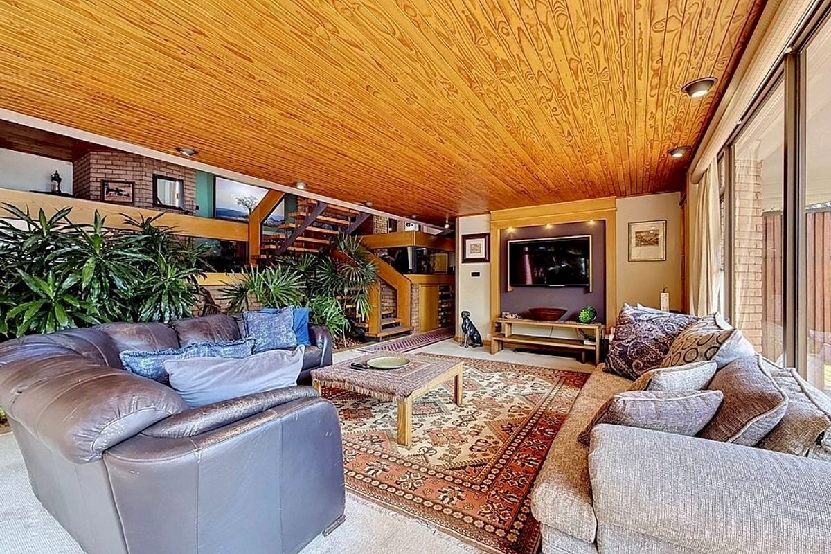 Spacious living room featuring a warm timber-clad ceiling, brick accents, and large sliding glass doors that provide ample natural light.
