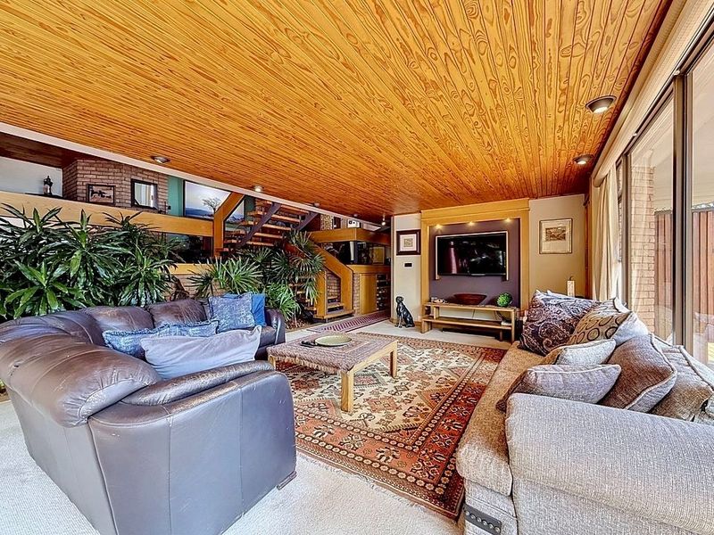 Spacious living room featuring a warm timber-clad ceiling, brick accents, and large sliding glass doors that provide ample natural light.