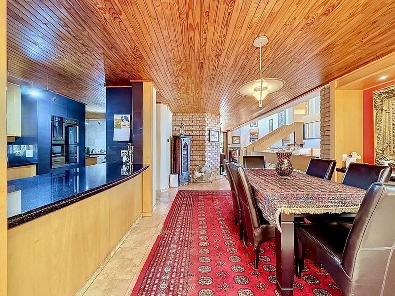 Open-plan kitchen and dining area featuring a distinctive timber-clad ceiling, granite countertops, and exposed brick architectural elements.