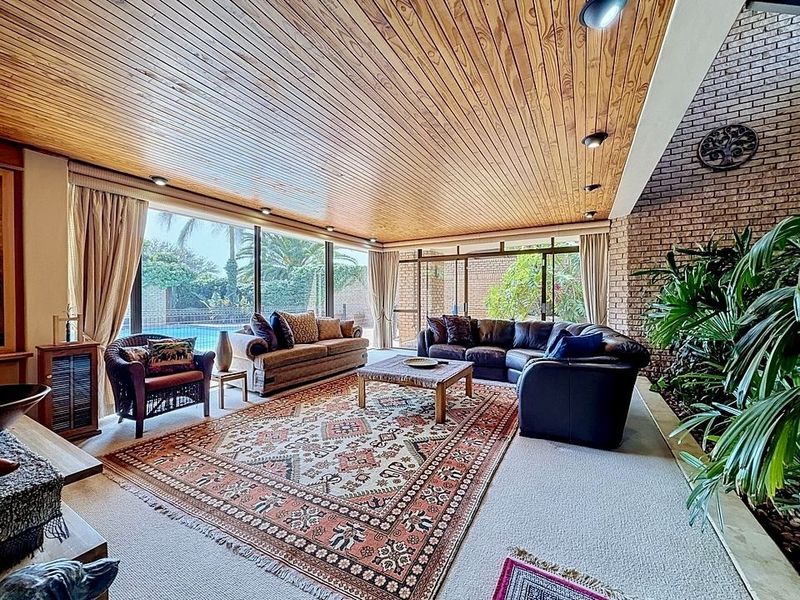 Spacious living room featuring a warm timber-clad ceiling, exposed brick feature wall, and large sliding glass doors providing views of the pool area.