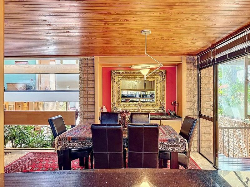 Dining room featuring a warm timber-clad ceiling, exposed brick accents, and large sliding glass doors providing natural light and garden views.