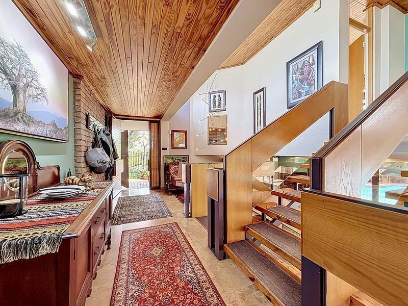 Spacious entrance hallway featuring a warm timber-clad ceiling, exposed brick accents, and a modern timber staircase with glass balustrades leading to upper levels.