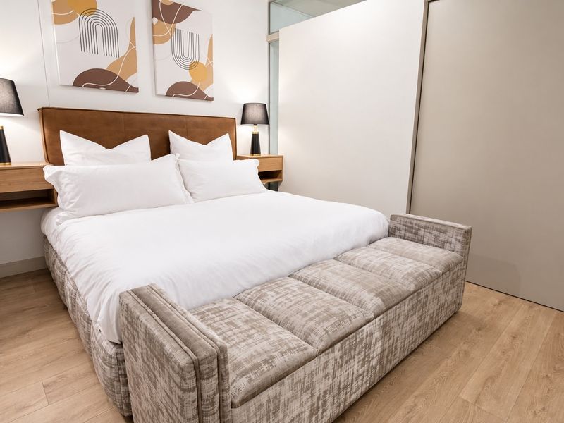 A well-maintained bedroom featuring modern laminate flooring, built-in bedside tables, and a neutral color palette.