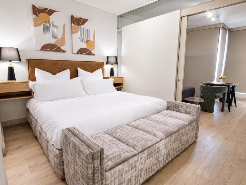 A modern, well-maintained bedroom featuring laminate flooring and a sleek sliding glass partition that opens into an adjacent living or dining space.