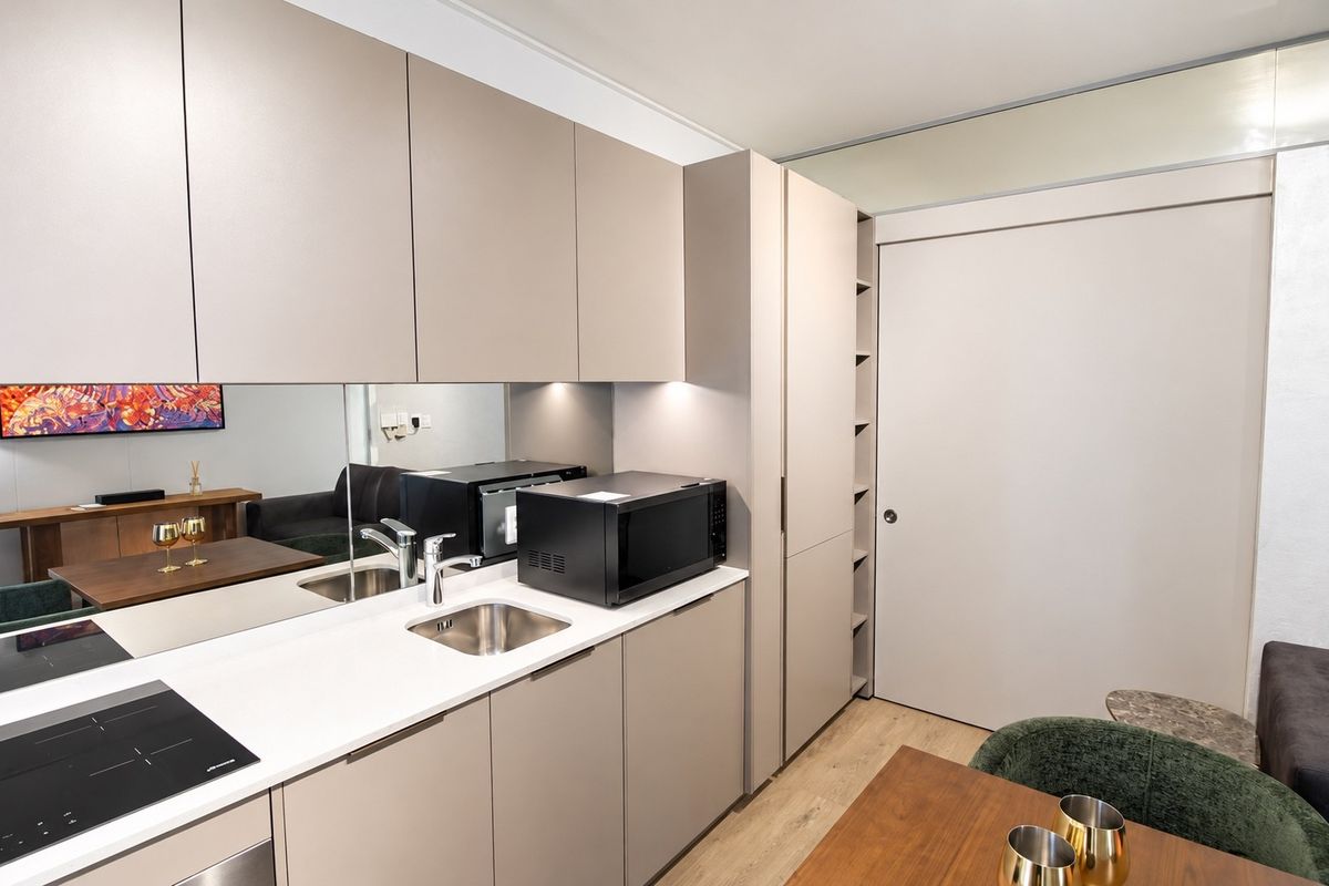 Modern compact kitchen featuring sleek handleless cabinetry, integrated sink, induction cooktop, and a mirrored backsplash, creating a clean and functional culinary space.