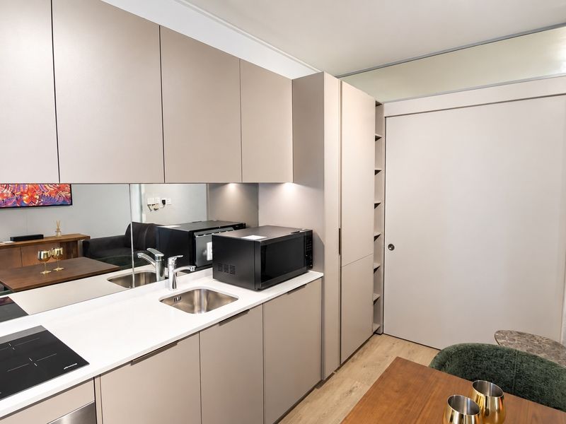 Modern compact kitchen featuring sleek handleless cabinetry, integrated sink, induction cooktop, and a mirrored backsplash, creating a clean and functional culinary space.