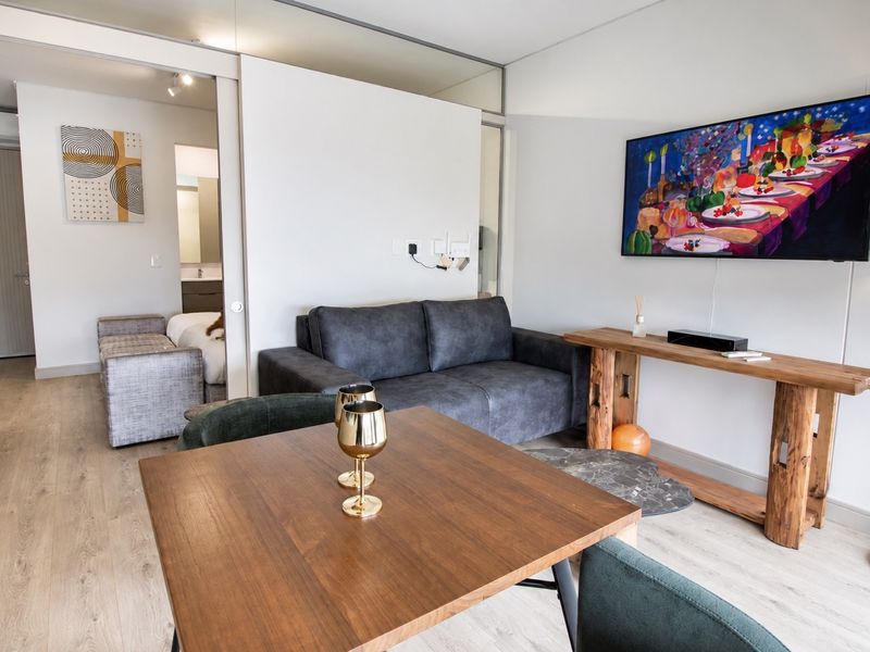 Modern open-plan living area featuring light laminate flooring and a sliding door leading to the bedroom suite.