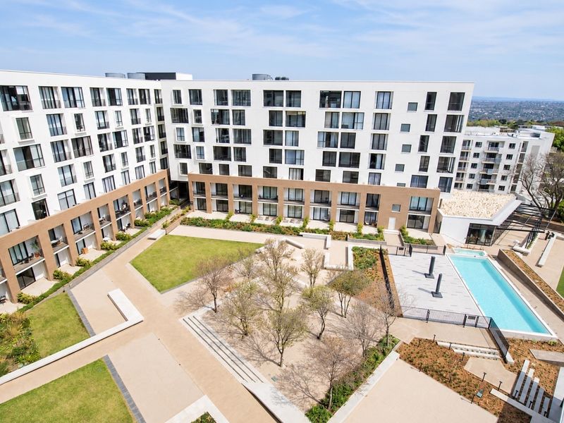 Aerial view of a modern apartment complex featuring a central landscaped courtyard, paved walkways, and a swimming pool area.