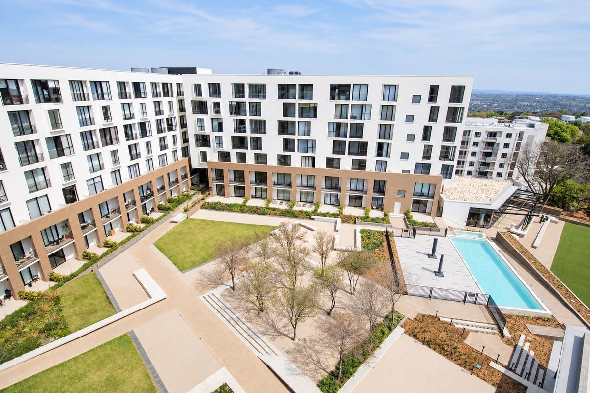 Aerial view of a modern apartment complex featuring a central landscaped courtyard, paved walkways, and a swimming pool area.