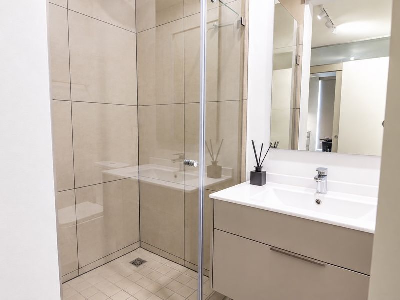 Modern bathroom featuring a glass-enclosed shower, sleek wall-mounted vanity with integrated basin, and neutral large-format tiling.