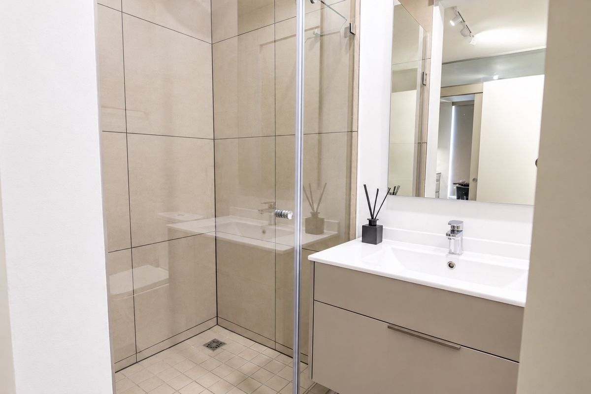 Modern bathroom featuring a glass-enclosed shower, sleek wall-mounted vanity with integrated basin, and neutral large-format tiling.