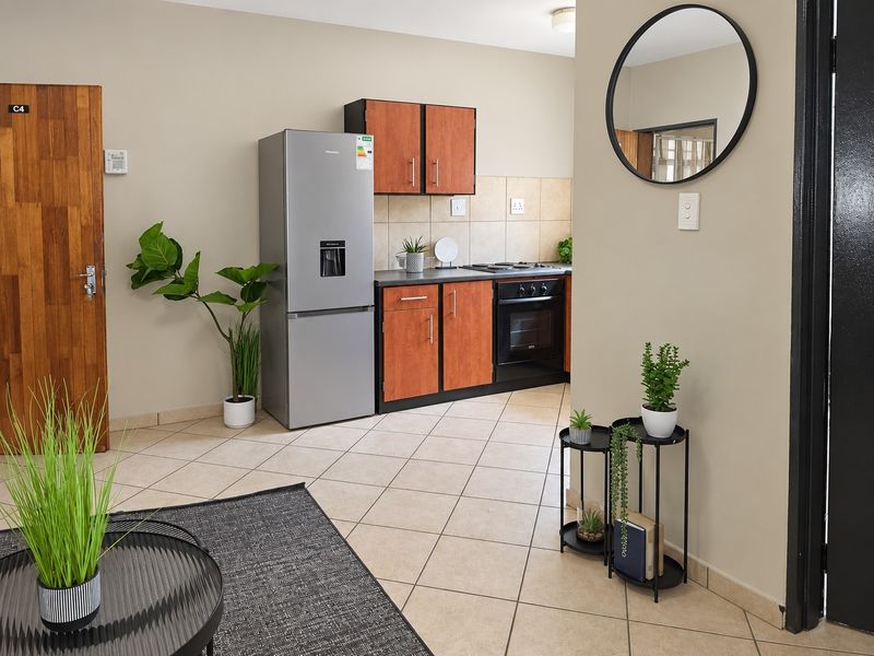 An open-plan living area featuring tiled flooring and a compact kitchen with built-in cabinetry, oven, and hob.