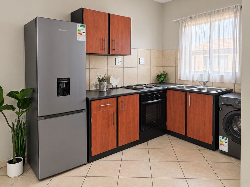 A functional kitchen featuring wood-finish cabinetry, dark countertops, ceramic tile backsplash, built-in oven, hob, and dedicated space for laundry appliances.