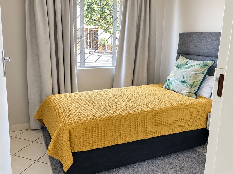 A well-lit bedroom featuring tiled flooring and a window fitted with security bars, offering a clean and functional living space.