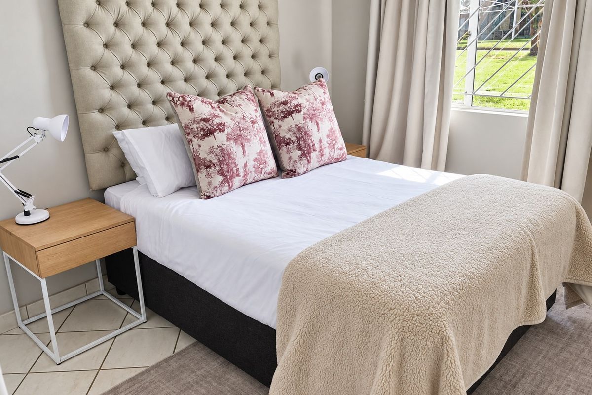 A well-maintained bedroom featuring tiled flooring and a window fitted with security bars, offering a clean and comfortable living space.