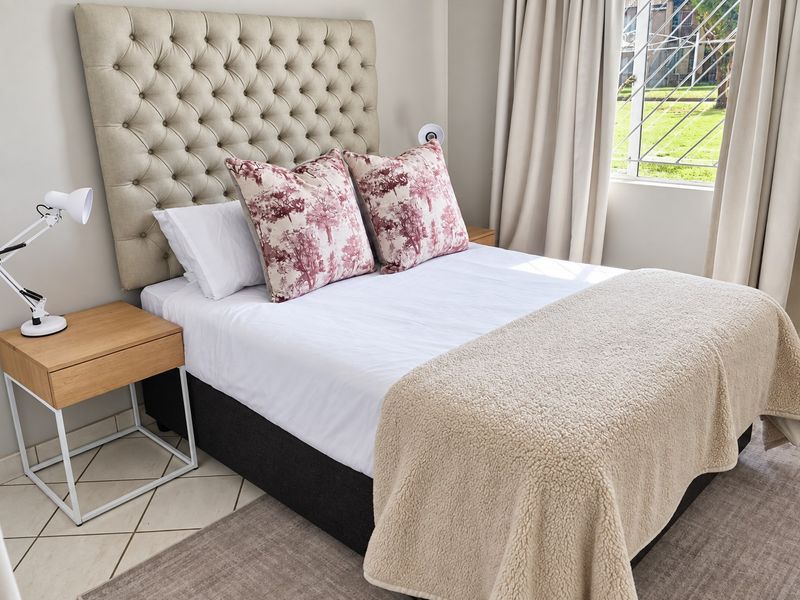 A well-maintained bedroom featuring tiled flooring and a window fitted with security bars, offering a clean and comfortable living space.