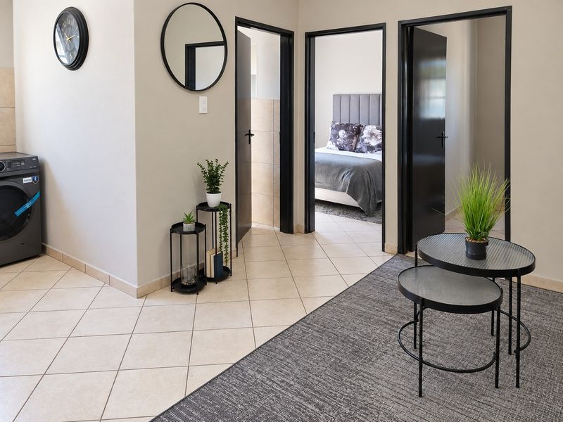 A well-maintained hallway featuring neutral tiled flooring and contrasting black door frames leading to adjacent rooms.