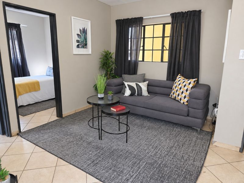 A cozy living room area featuring neutral wall tones, tiled flooring, and a window with security bars, providing a functional and comfortable living space.