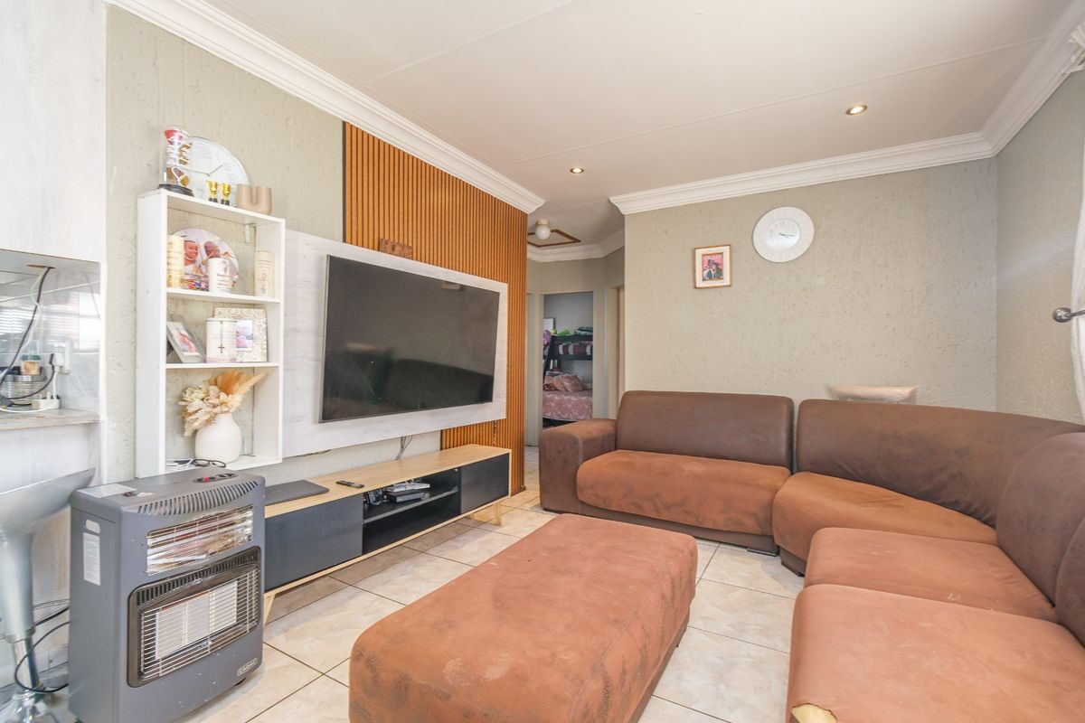 A living room featuring tiled flooring, coved ceilings with recessed lighting, and a decorative wood-slat feature wall.