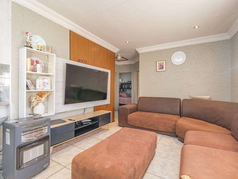 A living room featuring tiled flooring, coved ceilings with recessed lighting, and a decorative wood-slat feature wall.
